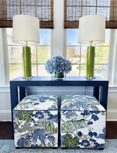 two blue and white stools in front of a window with flowers on top of them