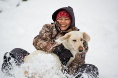 a woman riding on the back of a snowboard next to a dog in the snow