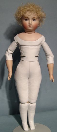 a doll with blonde hair is standing on a white base and has her hands in her pockets