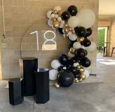 balloons and numbers are on display in front of the entrance to an apartment building, which is decorated with black, white and gold balloons