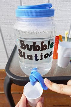 someone is holding a plastic cup in front of a bubble station sign on a table