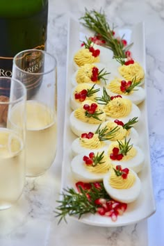 deviled eggs are arranged on a white platter next to two glasses of champagne