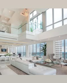 a living room filled with lots of white furniture and tall windows above the couches