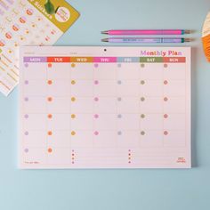 a calendar, pen and sticky pad on a desk with other items around the table