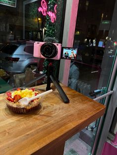 a wooden table topped with a bowl of fruit and a camera on top of it