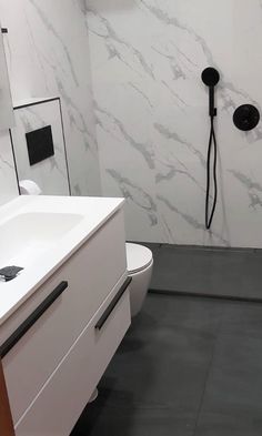 a bathroom with a toilet, sink and shower head mounted to the side of the wall