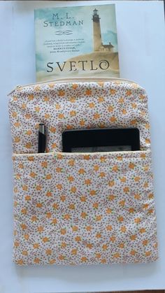 a book is sitting in the pocket of a small bag that has a phone inside it