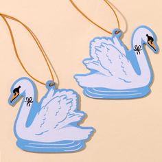 two blue swans are hanging from strings on a beige surface with an ornament in the shape of a bird