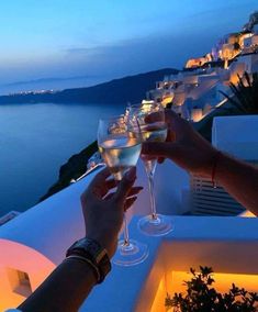 two people toasting with wine glasses on a balcony overlooking the ocean at night time