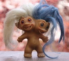 an odd looking troll doll with blue hair and long white hair standing next to another troll doll