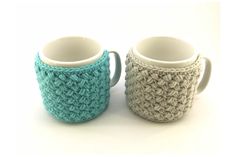 two crocheted coffee mugs sitting next to each other on a white surface