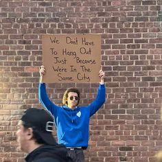 a man holding up a sign that says we don't have to hang out just because we were in the same city