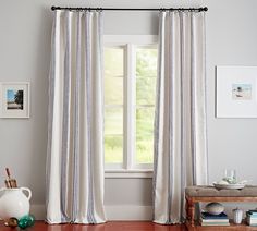 a living room with white walls and wooden floors, two windows covered in striped curtains