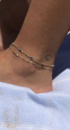 a woman's foot wearing a gold chain bracelet with evil eye charms on it