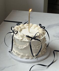 a white cake with a single candle on top and black ribbon around the edge, sitting on a table