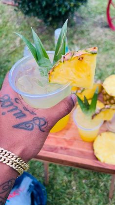 a person holding up a drink with pineapple on the table in the background,