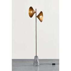 a floor lamp with two brass lamps on it and a white wall in the background