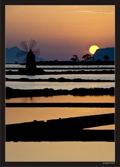 the sun is setting behind a windmill in the water