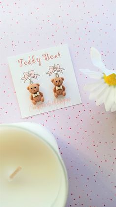 a pair of teddy bear earrings sitting on top of a table next to a candle