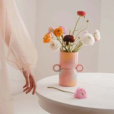 a vase with flowers in it sitting on a table next to a woman's hand