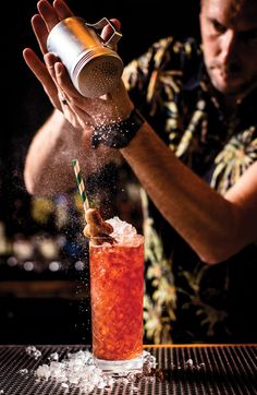 a man is pouring a drink into a tall glass with ice and sprinkles