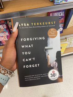 a person holding up a book in front of a shelf with several books on it