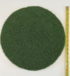 a large green grass covered circle next to a ruler