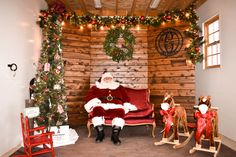 a santa clause sitting on a red couch in front of a christmas tree and rocking chair