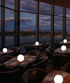 tables and chairs are set up in front of large windows overlooking the city at night