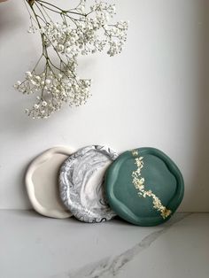 three plates sitting on top of a counter next to a vase with flowers in it