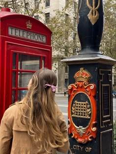 a woman standing next to a red phone booth in the middle of a city street