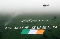 a helicopter flying over a green field with an irish flag