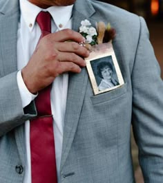 a man in a gray suit and red tie is holding a small photo on his lapel