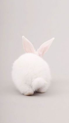 a white stuffed animal rabbit sitting on top of a floor next to a gray wall