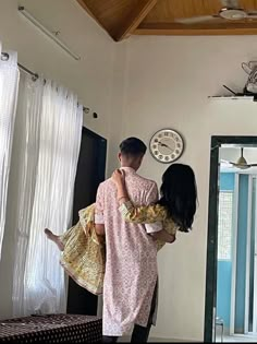 a man holding a woman in his arms while standing next to a clock on the wall