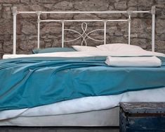 a white metal bed with blue sheets and pillows on top of it next to a brick wall