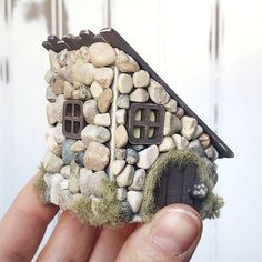 a small house made out of rocks and moss is held in the palm of someone's hand