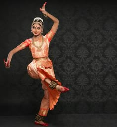 a woman in an orange and gold outfit is dancing with her arms out to the side