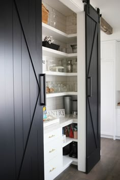 an open pantry door in a kitchen with white cupboards and black hardware on the doors