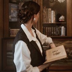 a woman holding an open book in front of a bookshelf filled with books