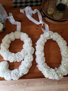 two wreaths made out of white flowers on a wooden table next to some candles