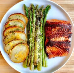 a white plate topped with asparagus, potatoes and meat on top of a wooden table