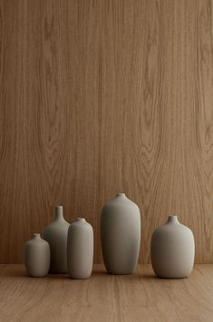 five white vases sitting on top of a wooden table in front of a wood wall