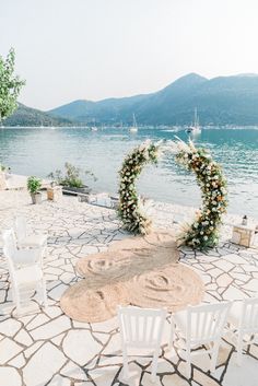 an outdoor ceremony setup with white chairs and flowers on the ground next to the water