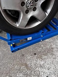 the tire is being worked on by a blue jacking device in front of a parked car