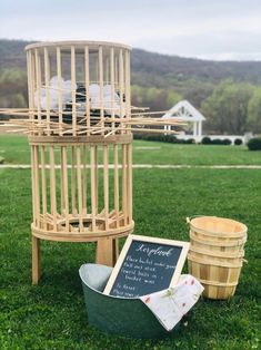 a wooden birdcage sitting on top of a lush green field next to two buckets