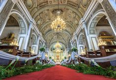 the interior of a large church with red carpet and white walls, chandeliers hanging from the ceiling