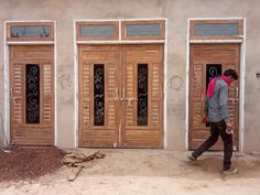 a man walking past two wooden doors in front of a building