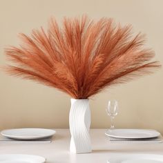 a white vase filled with lots of brown feathers on top of a dining room table