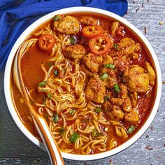 a bowl filled with noodles and meatballs on top of a wooden table next to a blue towel